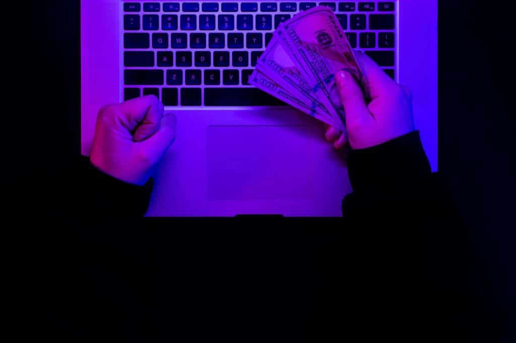 Hacker holding money while working on a laptop